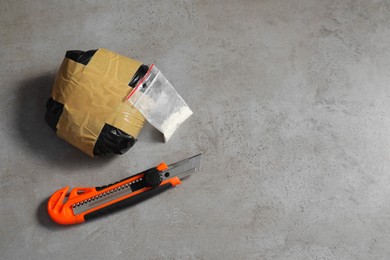 Photo of Packages with narcotics and stationery knife on grey textured table, flat lay. Space for text