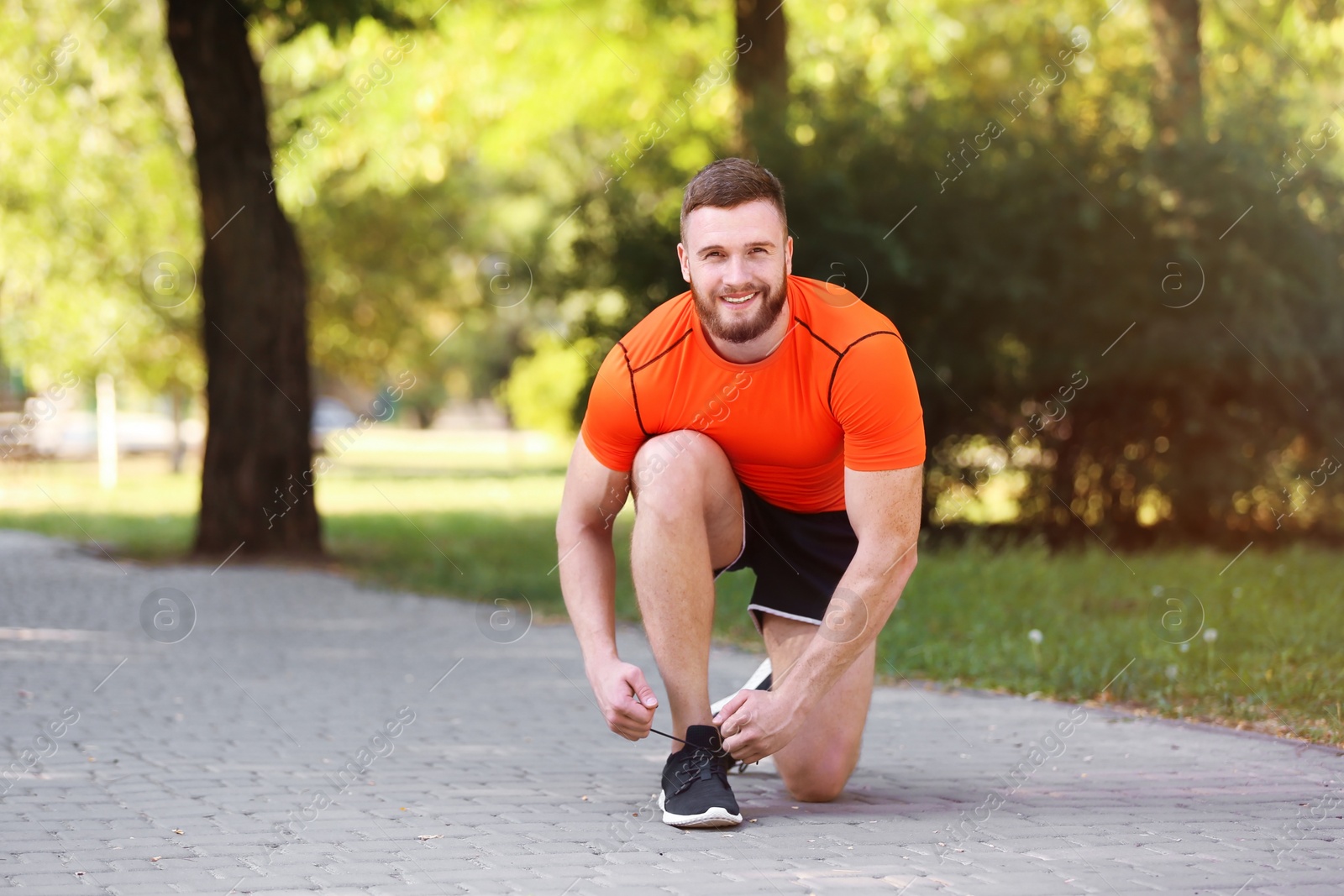 Photo of Young man tying shoelaces before running in park on sunny day