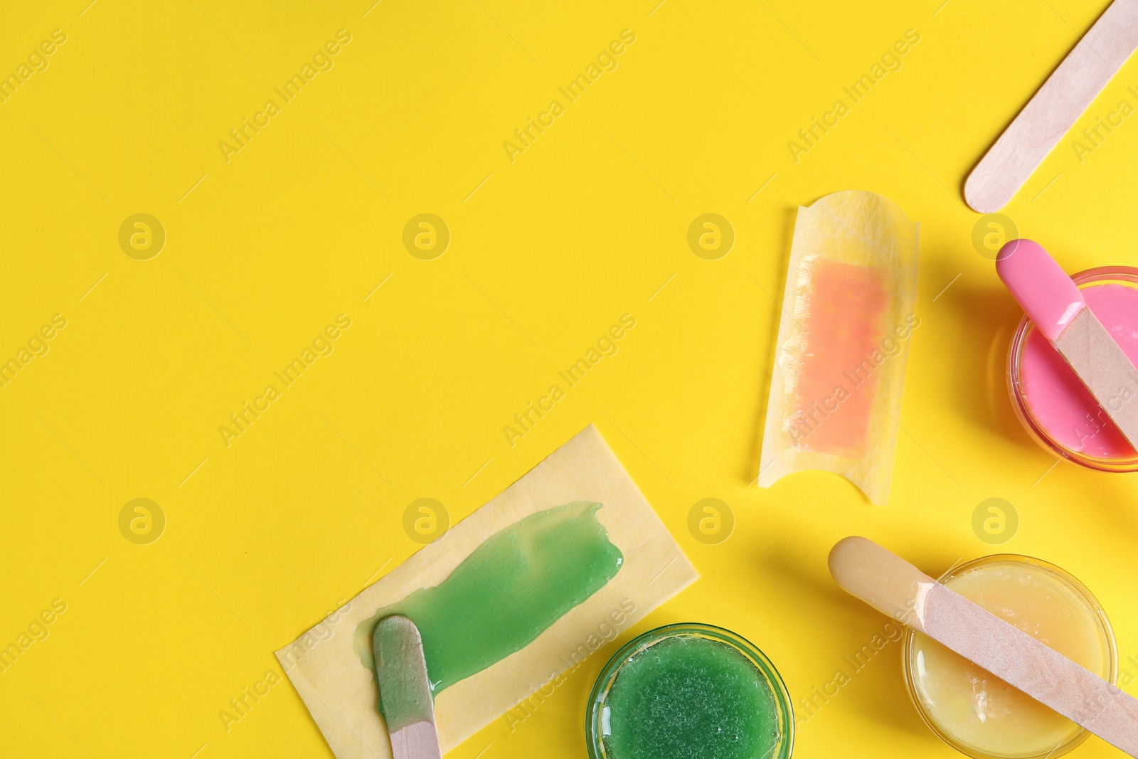 Photo of Flat lay composition with different types of wax and spatulas on yellow background. Space for text