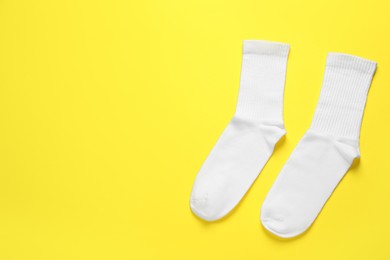 Photo of Pair of white socks on yellow background, flat lay. Space for text
