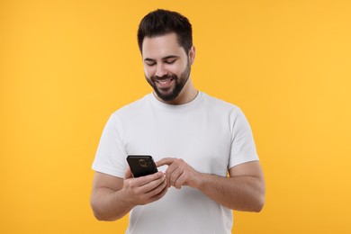 Happy young man using smartphone on yellow background