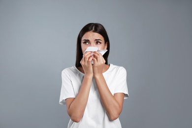 Young woman suffering from allergy on grey background