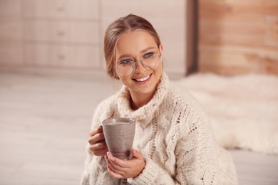 Beautiful young woman with cup of hot drink at home. Winter atmosphere
