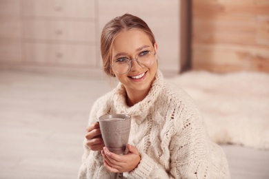 Photo of Beautiful young woman with cup of hot drink at home. Winter atmosphere