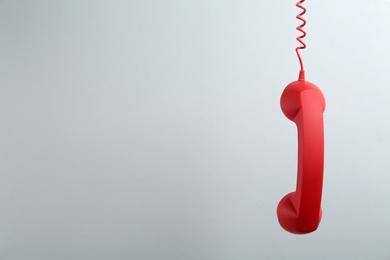 Photo of Red corded telephone handset hanging on light grey background, space for text. Hotline concept