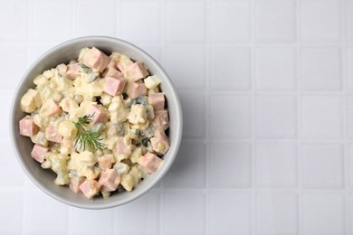 Photo of Tasty Olivier salad with boiled sausage in bowl on white tiled table, top view. Space for text