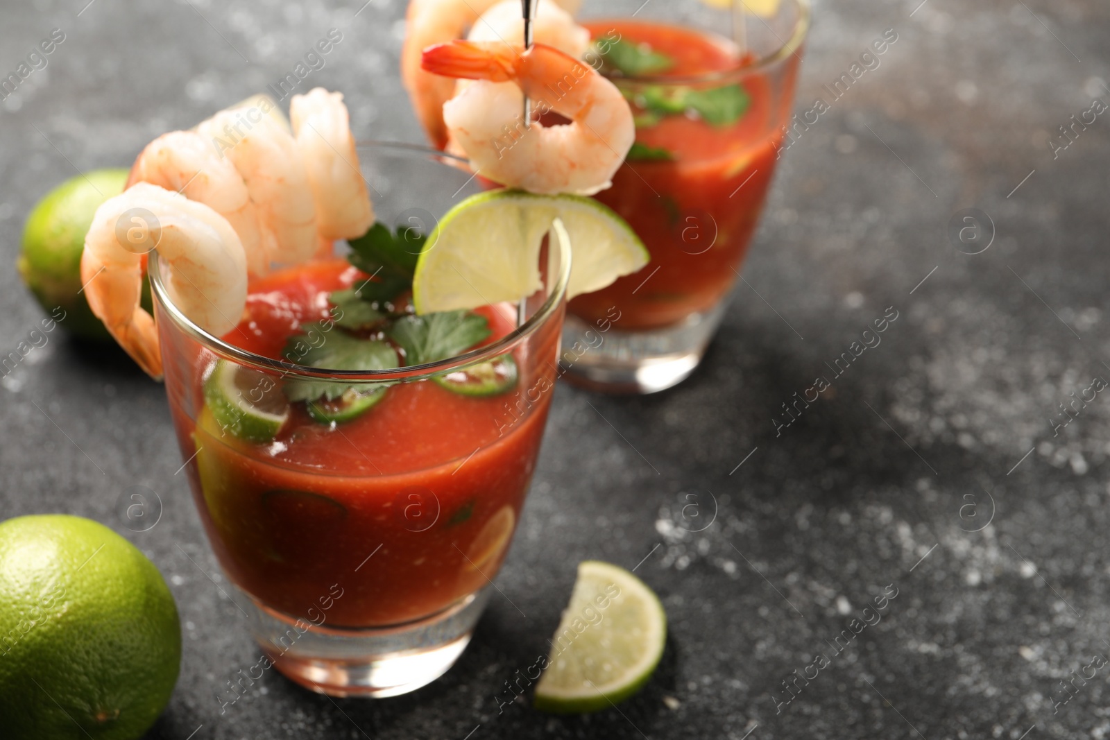 Photo of Tasty shrimp cocktail with sauce in glasses and lime on grey textured table, closeup. Space for text