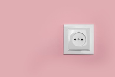 Power socket on pink wall, space for text. Electrical supply