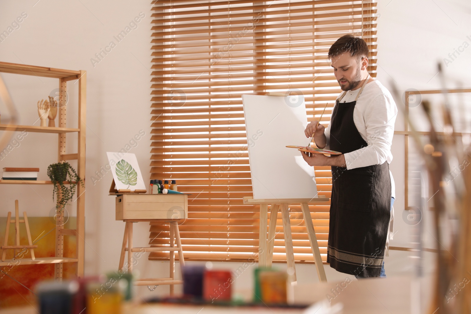 Photo of Young man painting on easel with brush in artist studio