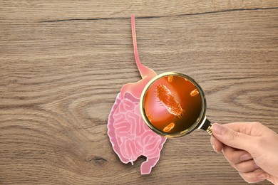 Microorganisms research. Woman with magnifying glass and paper intestine cutout on wooden background, top view