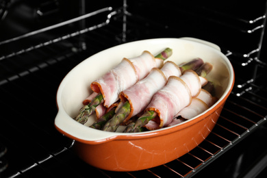 Photo of Uncooked bacon wrapped asparagus in baking dish on oven rack, closeup