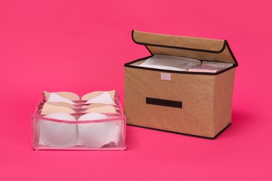 Photo of Textile storage case and organizer with bras on pink background
