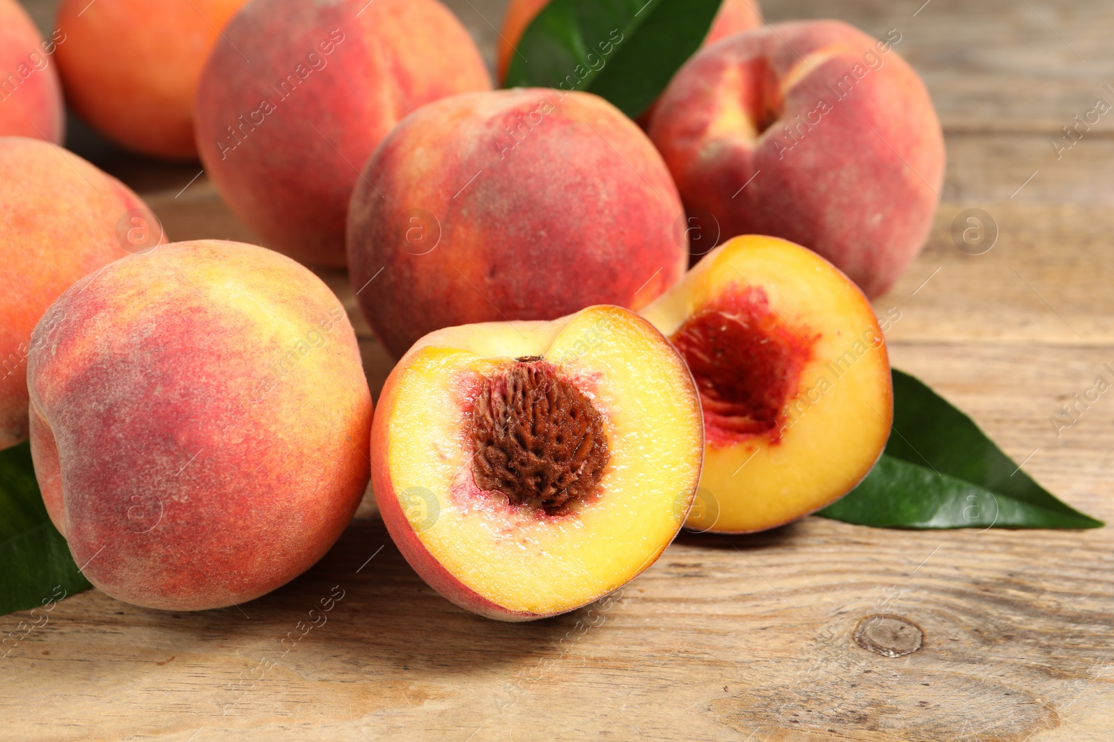 Photo of Cut and whole fresh ripe peaches with green leaves on wooden table, closeup