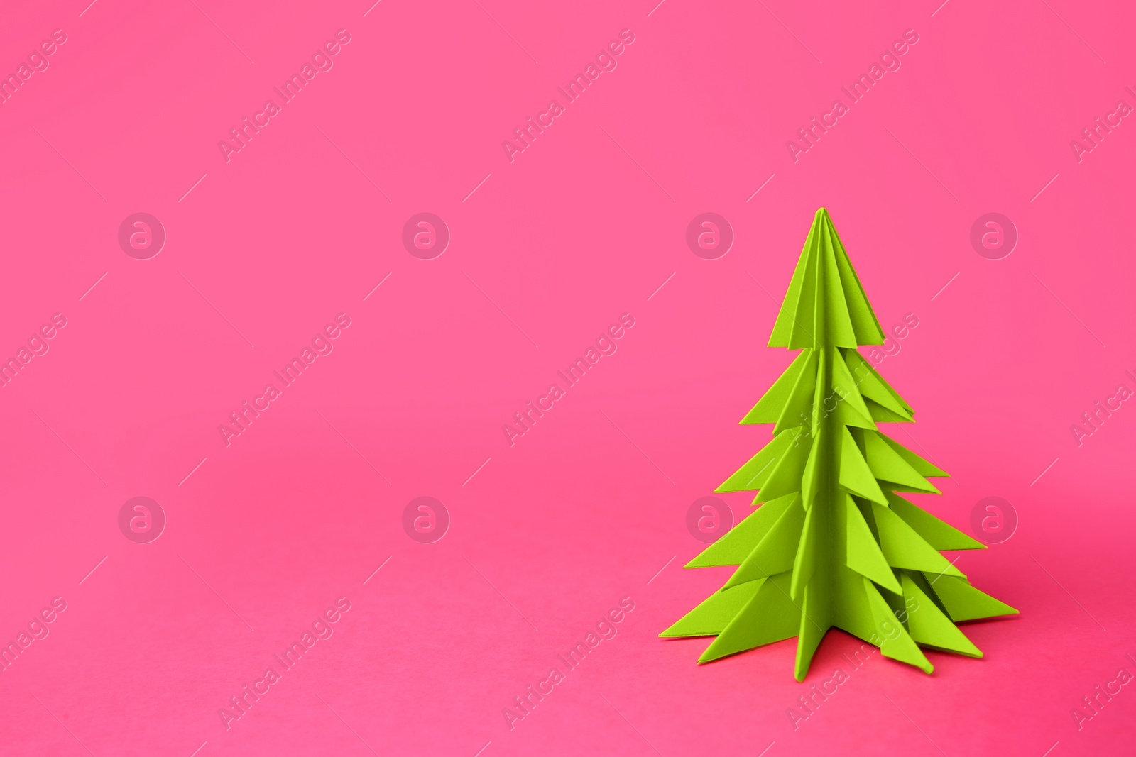 Photo of Origami art. Handmade paper Christmas tree on pink background, space for text