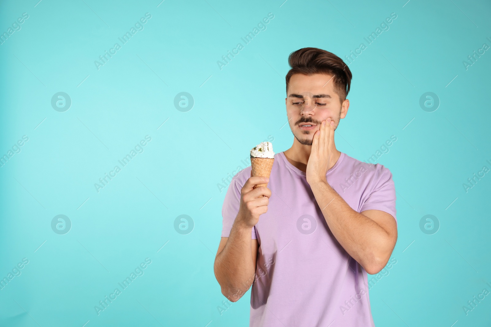 Photo of Young man with sensitive teeth and ice cream on color background. Space for text