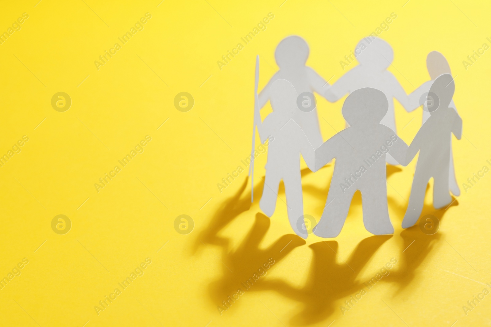 Photo of Paper people chain making circle on yellow background, space for text. Unity concept