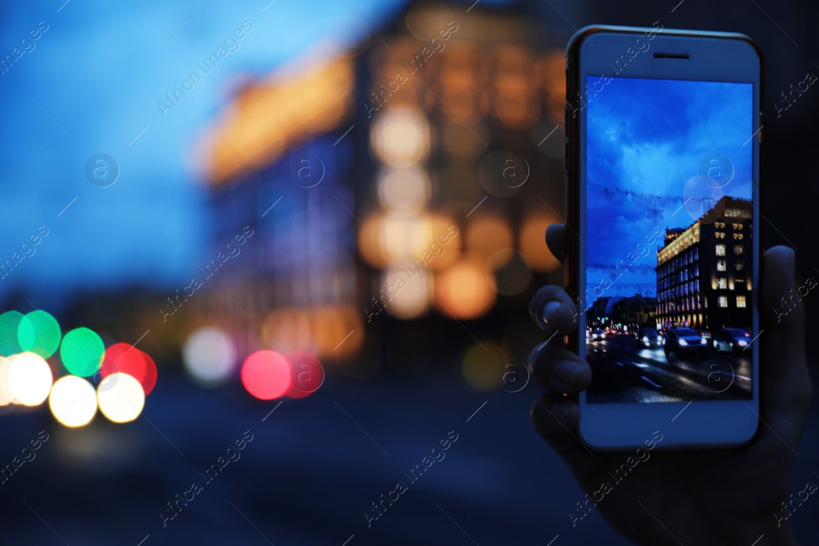 Photo of Woman taking photo of modern city in evening with smartphone, focus on hand. Bokeh effect