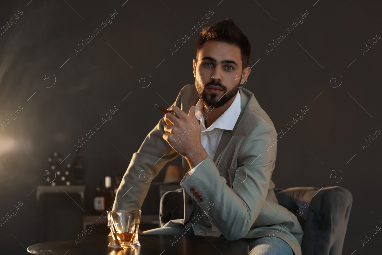 Photo of Man with glass of whiskey and cigar sitting at table indoors