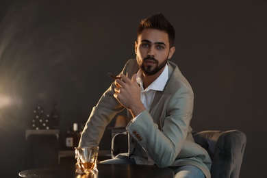 Photo of Man with glass of whiskey and cigar sitting at table indoors