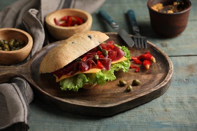 Photo of Delicious sandwich with bresaola, cheese and lettuce served on light blue wooden table