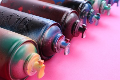 Photo of Many spray paint cans on pink background, closeup
