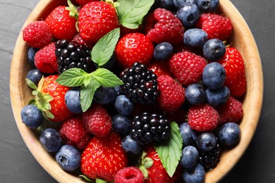 Photo of Many different fresh ripe berries in wooden bowl on black table, top view