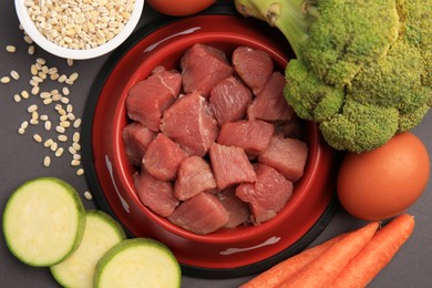 Photo of Raw meat in bowl and healthy products for pet on black background, flat lay