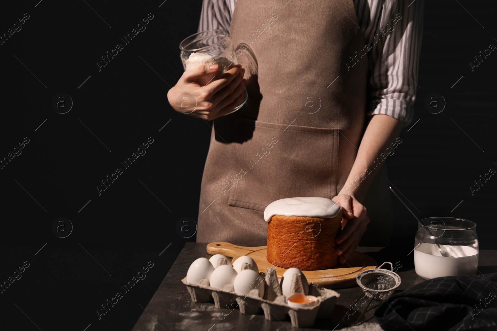 Photo of Young woman making traditional Easter cake at table against black background, closeup. Space for text