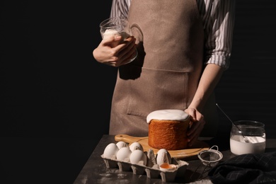 Photo of Young woman making traditional Easter cake at table against black background, closeup. Space for text