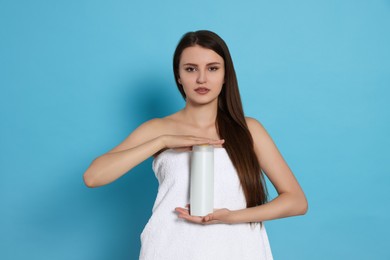 Photo of Beautiful young woman wrapped in towel holding bottle of shampoo on light blue background