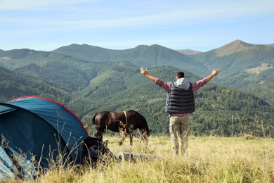 Photo of Man and horse near camping tent in mountains, back view