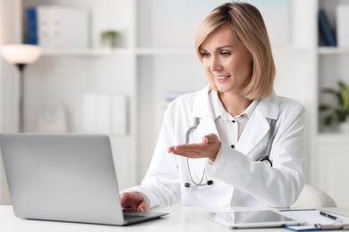 Photo of Smiling doctor with laptop having online consultation at table in office