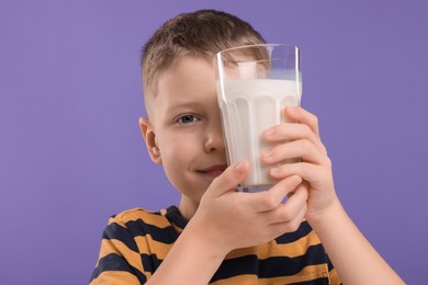 Photo of Cute boy with glass of fresh milk on violet background
