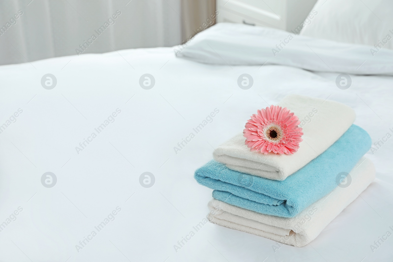 Photo of Stack of clean towels with flower on bed indoors. Space for text