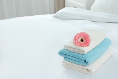 Stack of clean towels with flower on bed indoors. Space for text