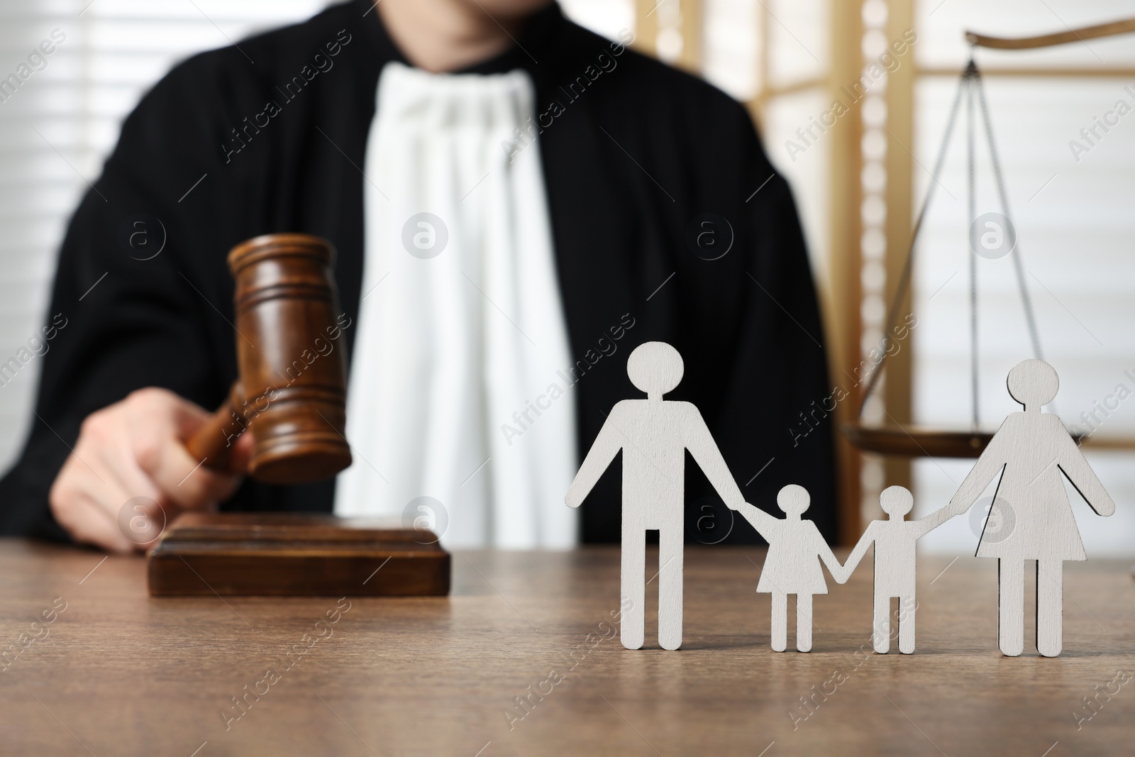 Photo of Family law. Judge with gavel sitting at wooden table, focus on figure of parents and children