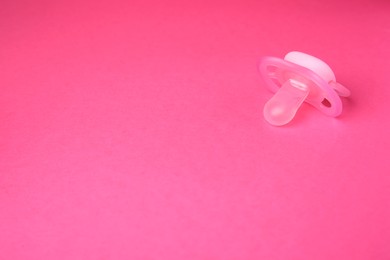 Photo of One baby pacifier on pink background. Space for text