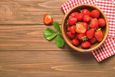 Bowl with ripe strawberries on wooden background, top view