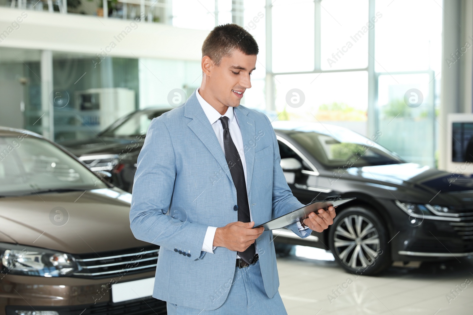 Photo of Young salesman with clipboard in modern car dealership