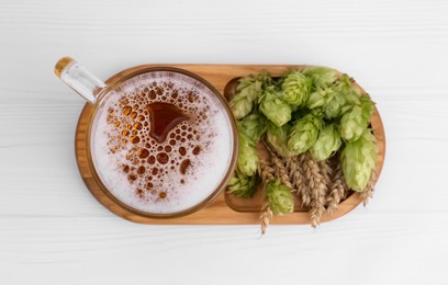 Mug with beer, fresh hops and ears of wheat on white wooden table, top view
