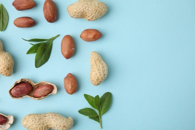 Photo of Fresh peanuts and leaves on light blue table, flat lay. Space for text