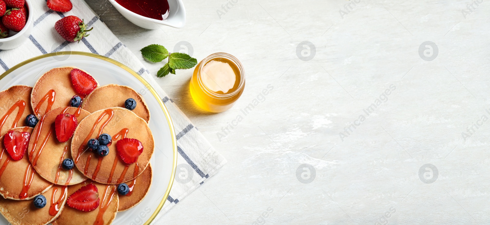 Image of Tasty pancakes with berries served on light table, flat lay. Banner design, space for text 