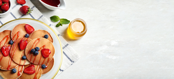 Tasty pancakes with berries served on light table, flat lay. Banner design, space for text 