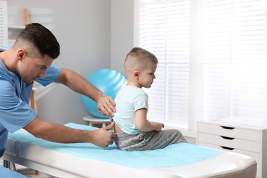 Photo of Orthopedist examining child's back in clinic. Scoliosis treatment