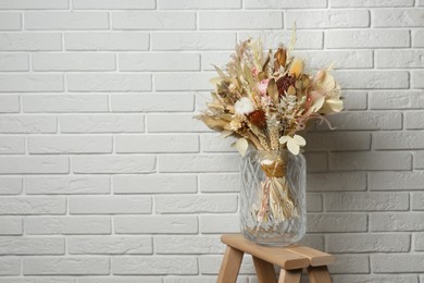 Beautiful dried flower bouquet in glass vase on wooden ladder near white brick wall. Space for text