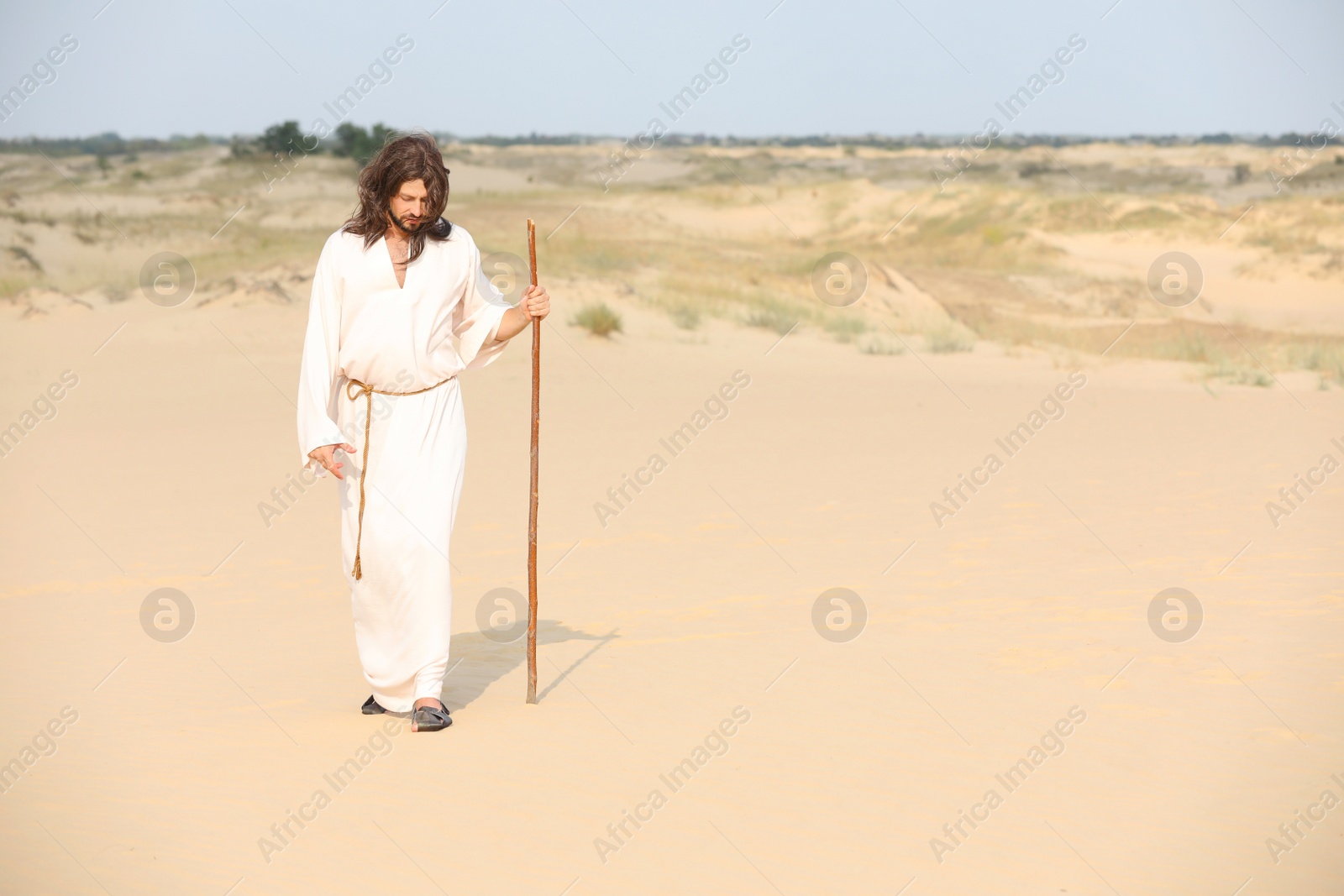 Photo of Jesus Christ walking with stick in desert. Space for text