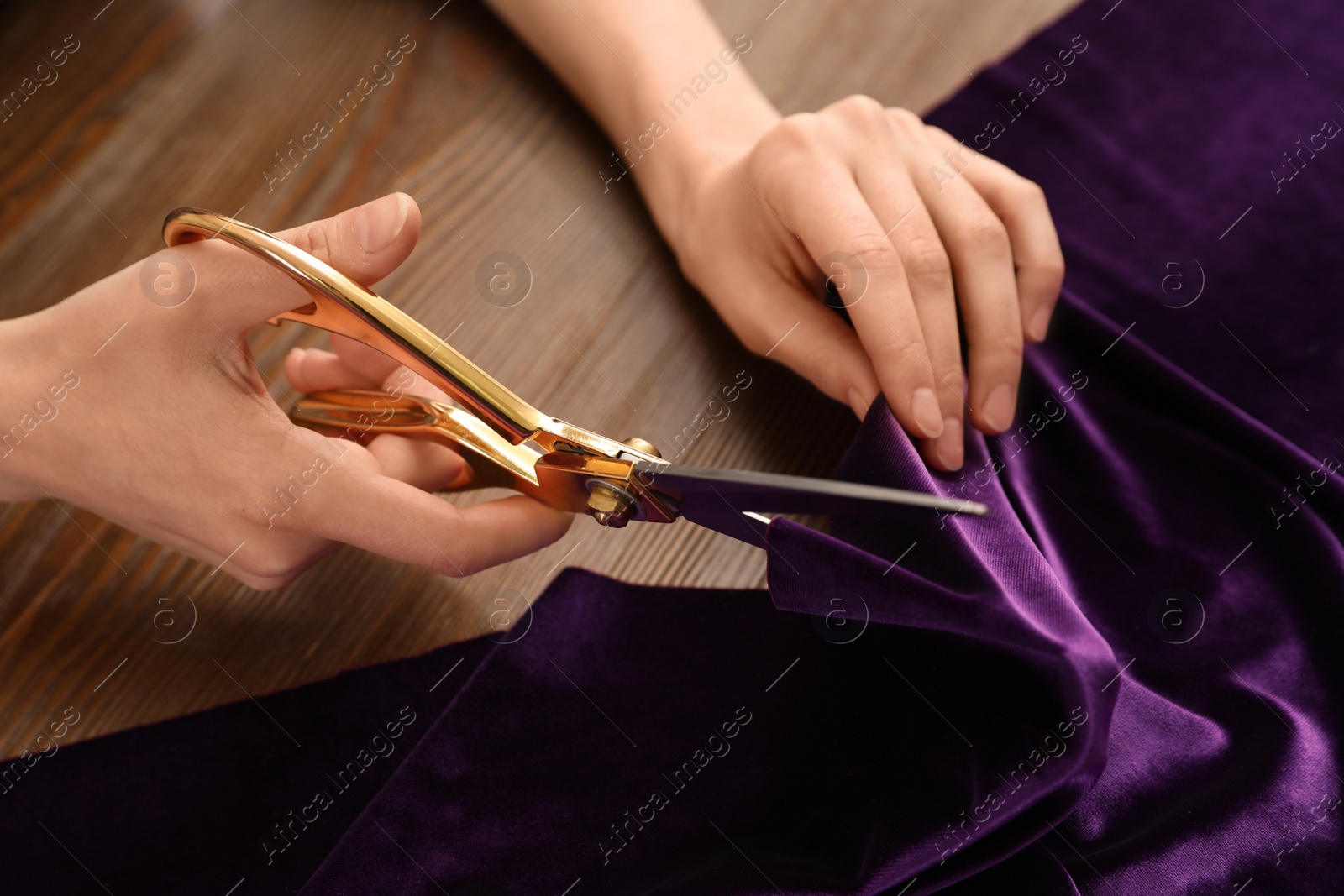 Photo of Woman cutting fabric with sharp scissors at wooden table, closeup