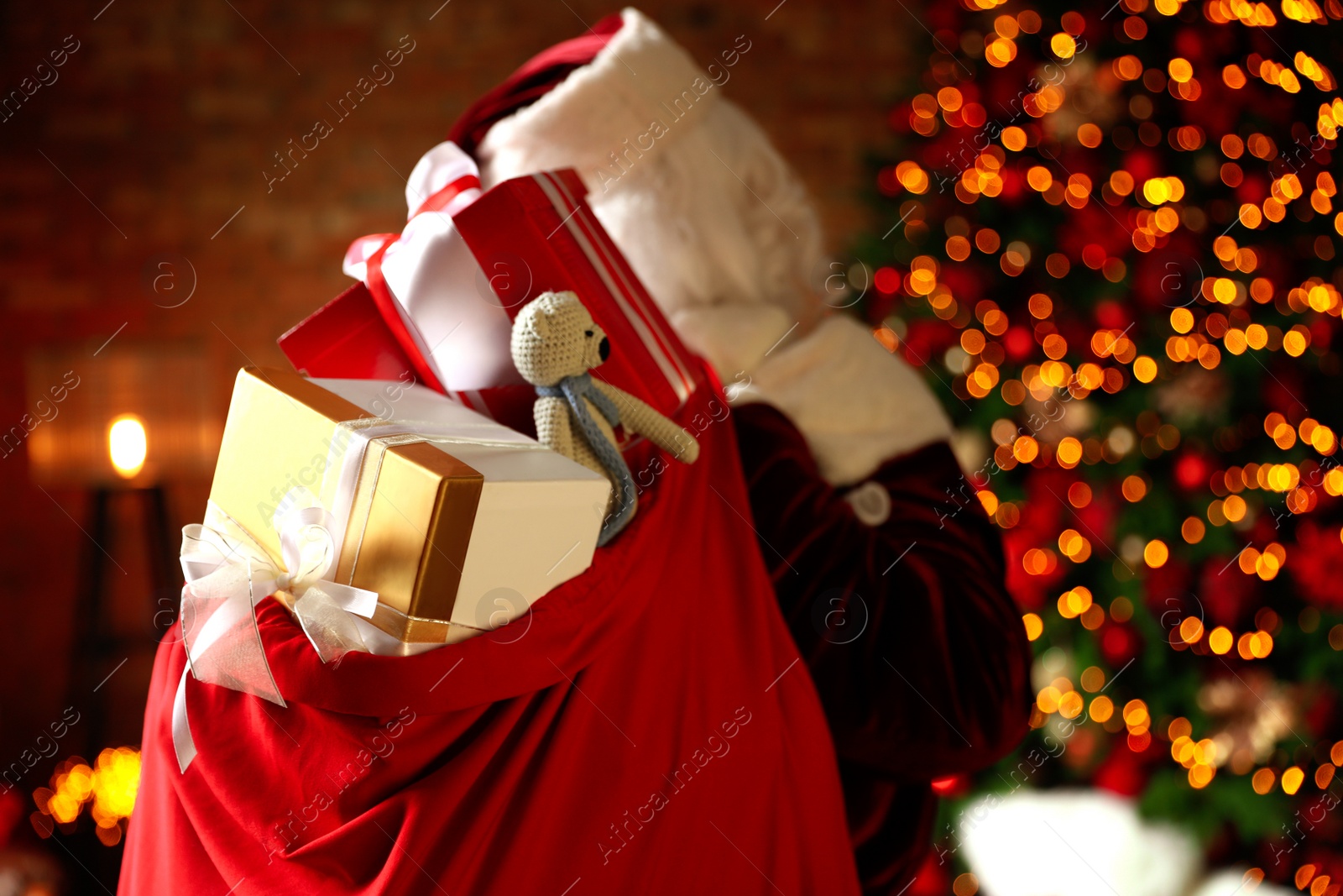 Photo of Santa Claus holding bag full of Christmas gifts against blurred festive lights