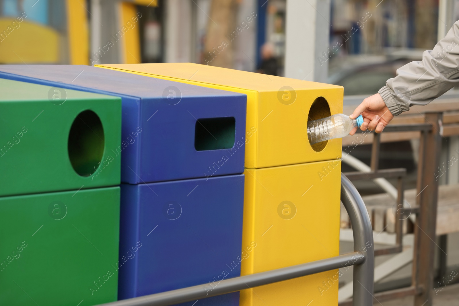 Photo of Man throwing plastic bottle into garbage bin outdoors, closeup. Waste sorting