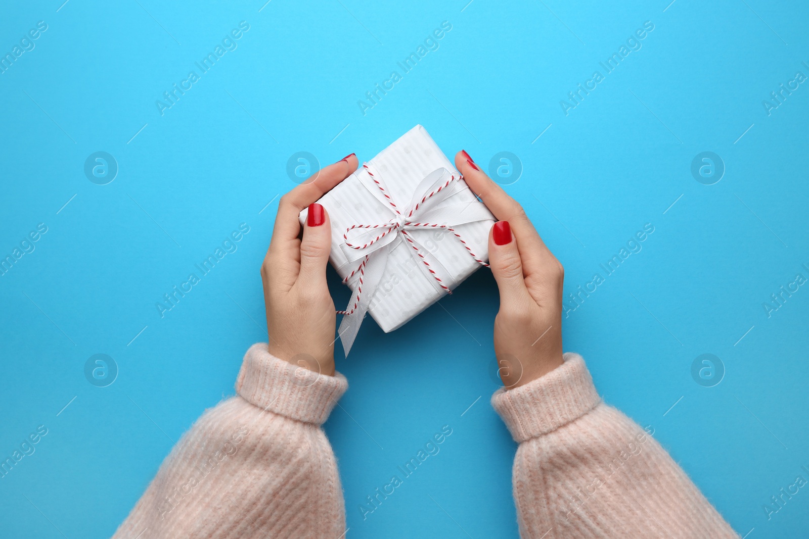 Photo of Woman holding Christmas gift box on light blue background, top view